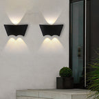 A pair of the black sconces lit side by side above a concrete bench, next to a glazed door.
