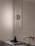 Clérachic wall sconce seen from a wider bathroom angle, its brass bar reflected in the mirror above a marble vanity.