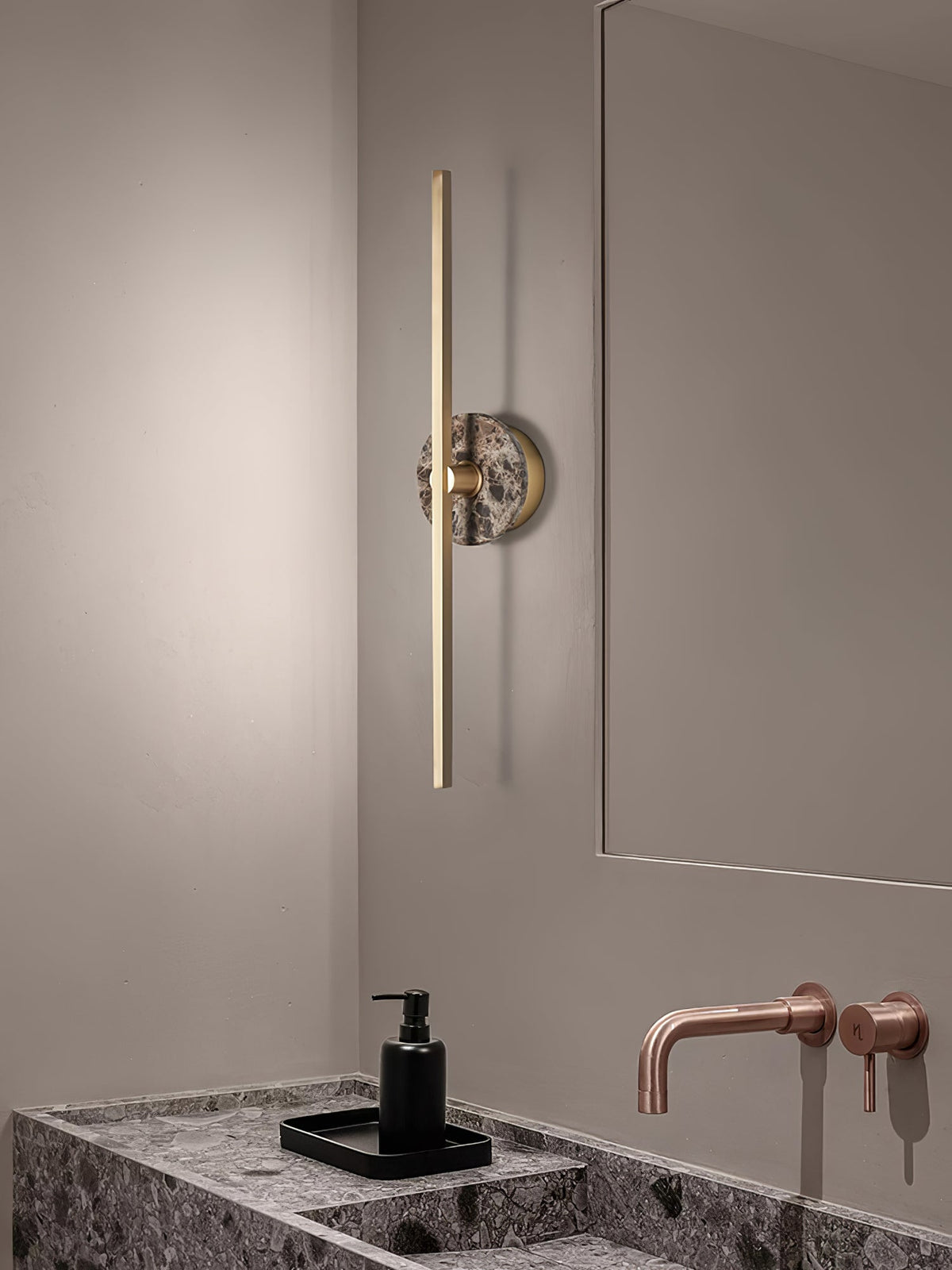 Clérachic wall sconce seen from a wider bathroom angle, its brass bar reflected in the mirror above a marble vanity.