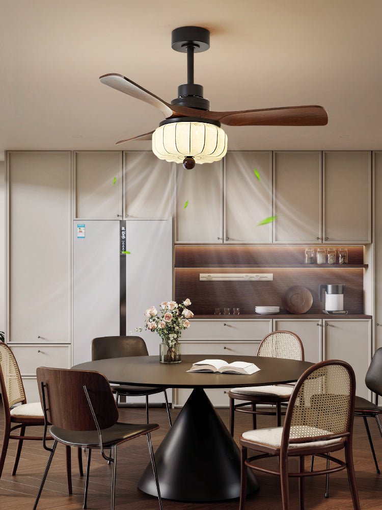A tighter crop shows this Clérachic ceiling fan's lantern shade lit above a cone-based dining table with a flower vase and cane chairs.