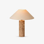 The Clérachic table lamp shown alone on a plain grey background, its beige fabric shade lit warmly above the marble column.