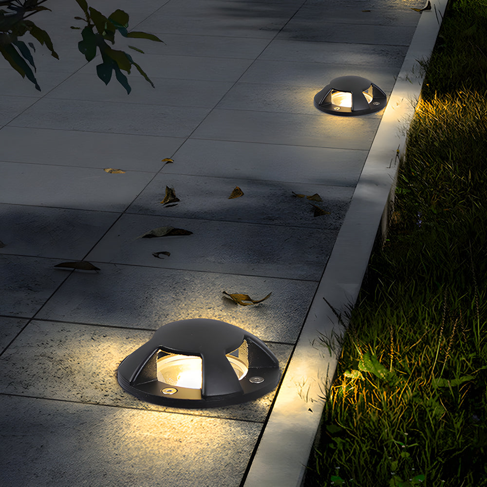 Two domed lights lit on paving beside grass, fallen leaves scattered around the beams.