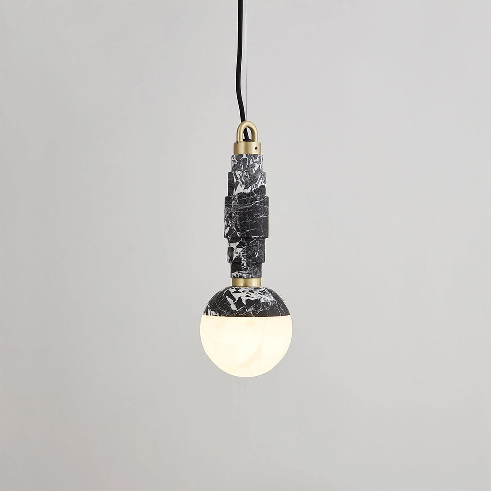 Angled view of the black-and-white marble pendant lit, brass collar visible where the stem meets the globe.