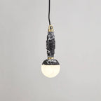 Angled view of the black-and-white marble pendant lit, brass collar visible where the stem meets the globe.