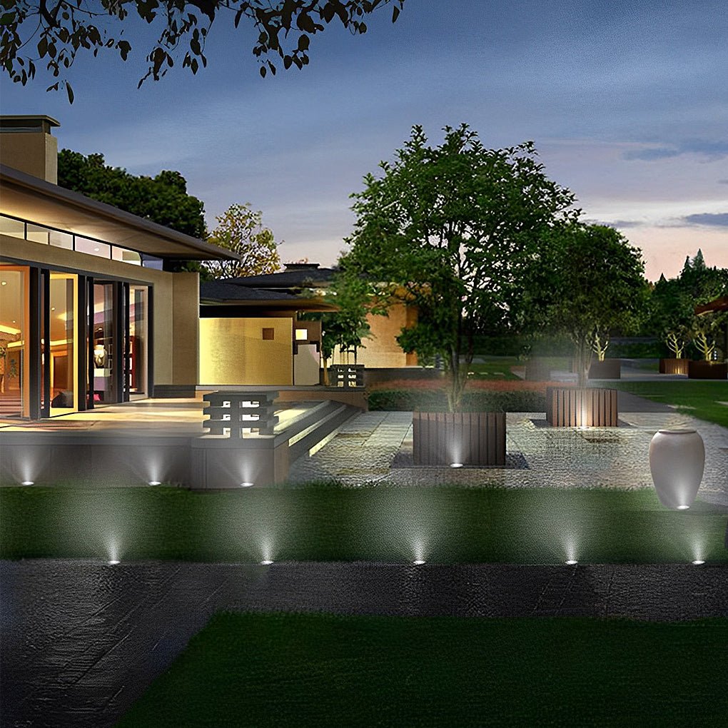 Inground lights lit in a row along a garden path edge at dusk, with a modern house beyond.
