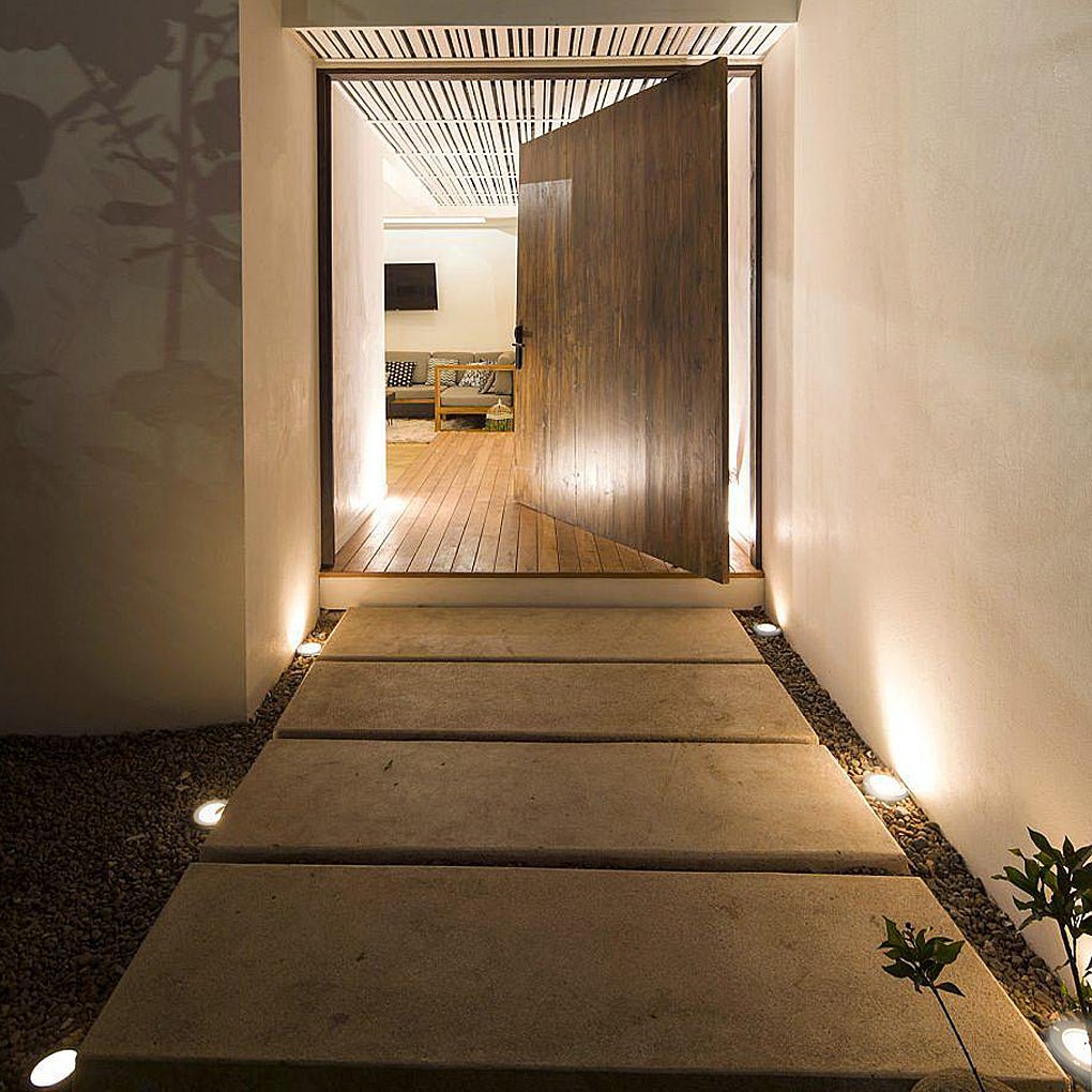 Recessed step lights lit along a concrete entrance path at night, leading to an open timber pivot door.