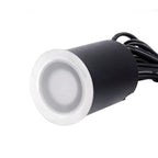 Close view of a single unlit step light, its frosted lens set in a steel ring above the black body and cable.