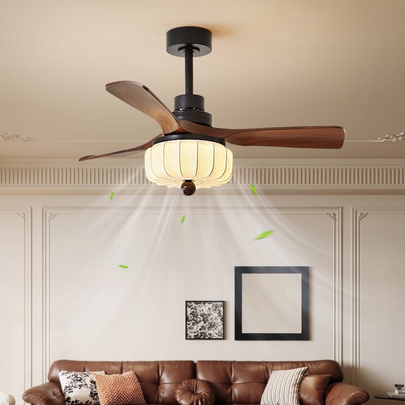 Walnut fan blades and a lit lantern shade hang above a brown leather sofa with framed art on the wall, this Clérachic ceiling fan warms the room.