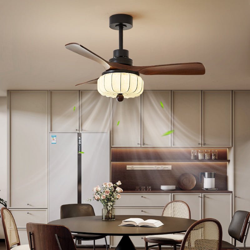 Above a round dining table set with an open book and a vase of flowers, this Clérachic fan's cream lantern shade glows against walnut cabinetry.