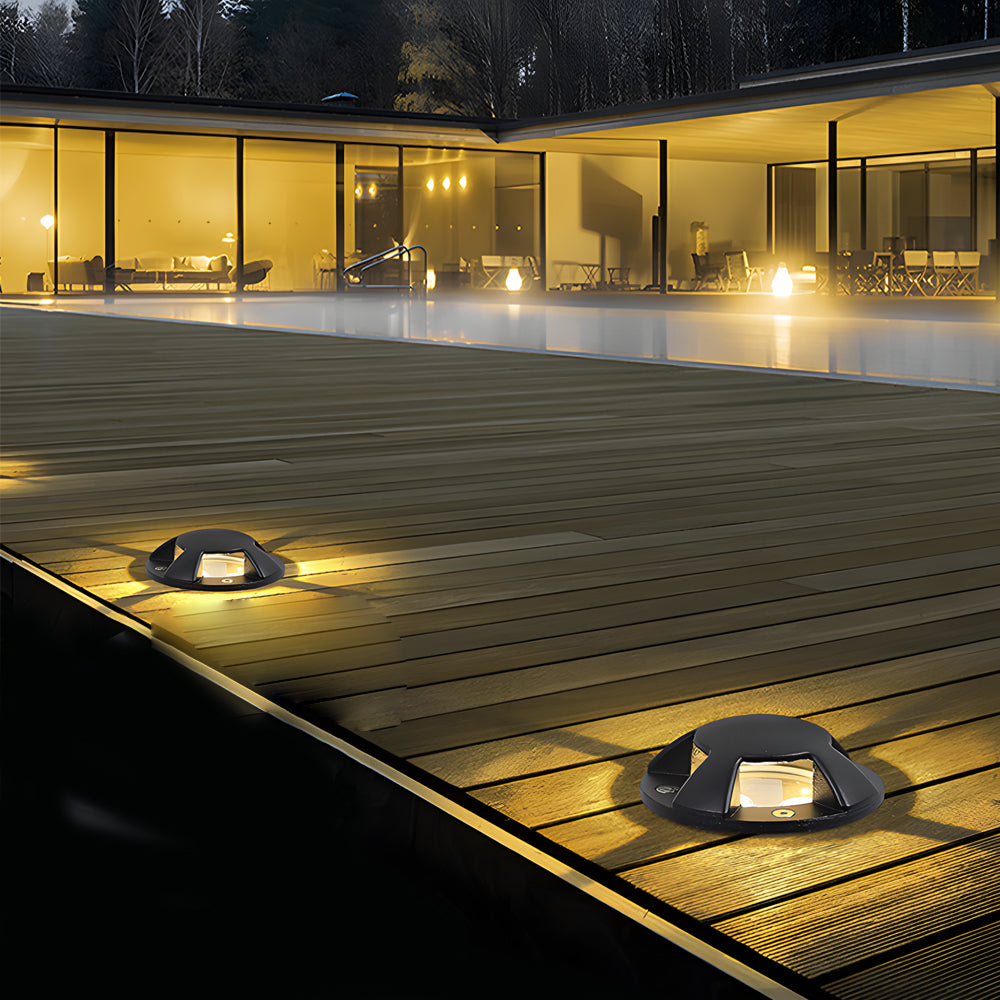 Two domed deck lights lit in timber decking at night, in front of a glazed modern house.
