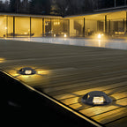 Two domed deck lights lit in timber decking at night, in front of a glazed modern house.
