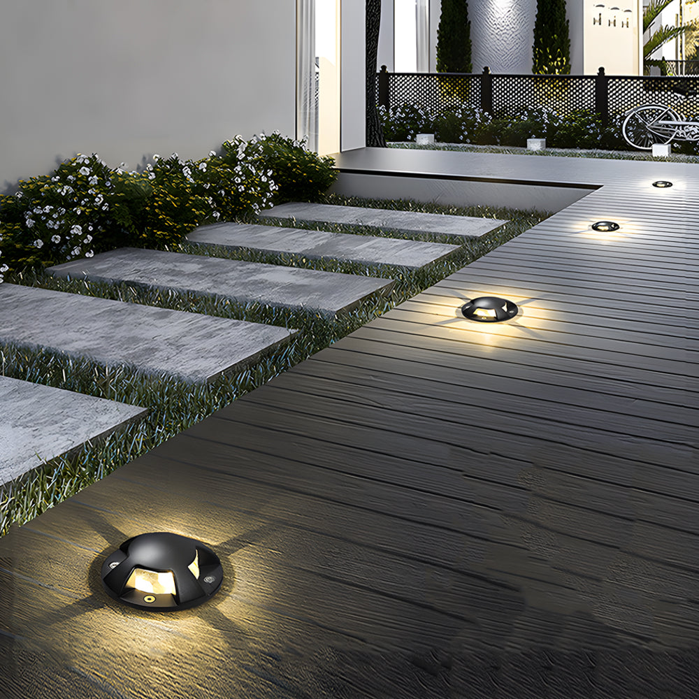 Several domed deck lights lit into timber decking at night, beside stone steps and planting.