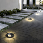 Several domed deck lights lit into timber decking at night, beside stone steps and planting.