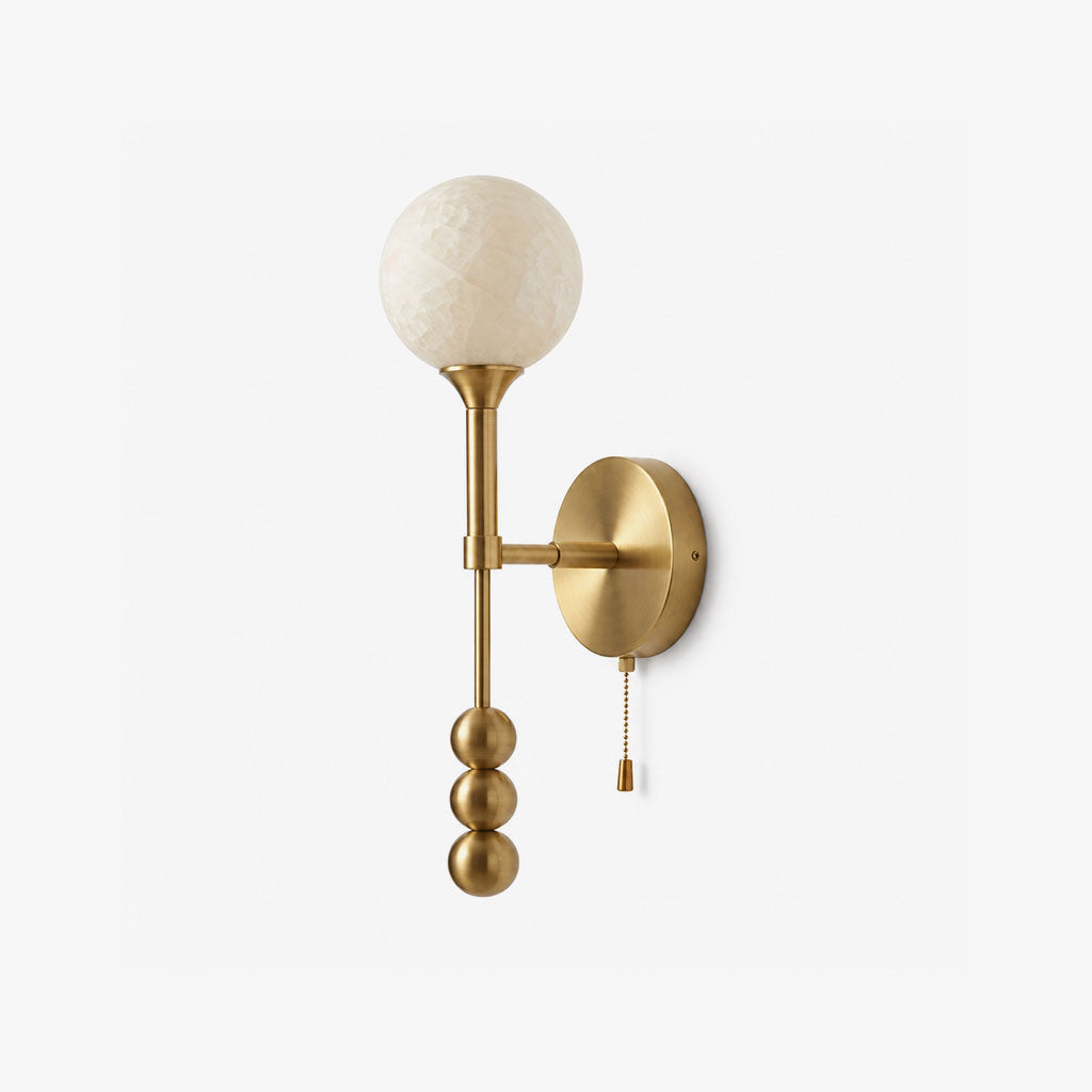 Studio view of this Clérachic wall sconce in brushed brass, its round alabaster ball shade topping a diagonal rod.