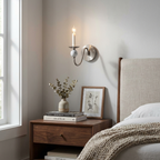 Above a wood nightstand with a small vase and stacked books, this Clérachic wall light glows in a brushed-nickel finish.