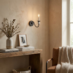 Near an armchair draped with a plaid throw, this Clérachic wall light glows in matte black above a console table.