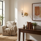 Beside a linen armchair and a console table of books, this Clérachic wall light glows in a brass finish.