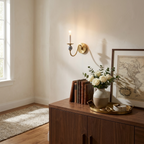 Over a console table topped with a vase of roses and a framed map, this Clérachic wall light glows in a brass finish.