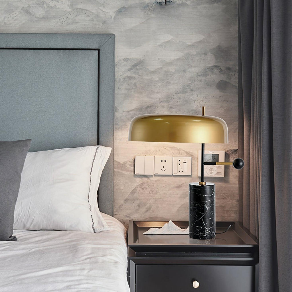 Lit against a grey wall with visible light switches, the Clérachic lamp sits on a black nightstand beside a bed.