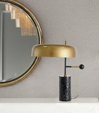 The Clérachic table lamp sits beside a round gold-framed mirror on a table against a textured grey wall.