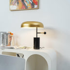 Switched on, this Clérachic table lamp casts a warm glow over books and a small vase on a curved white nightstand.