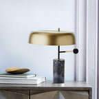 The Clérachic table lamp rests on a metallic-textured nightstand beside stacked books and a small stone dish.