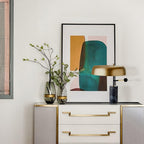 The Clérachic gold dome lamp lights a beige dresser with gold drawer pulls, framed art and glass vases behind it.