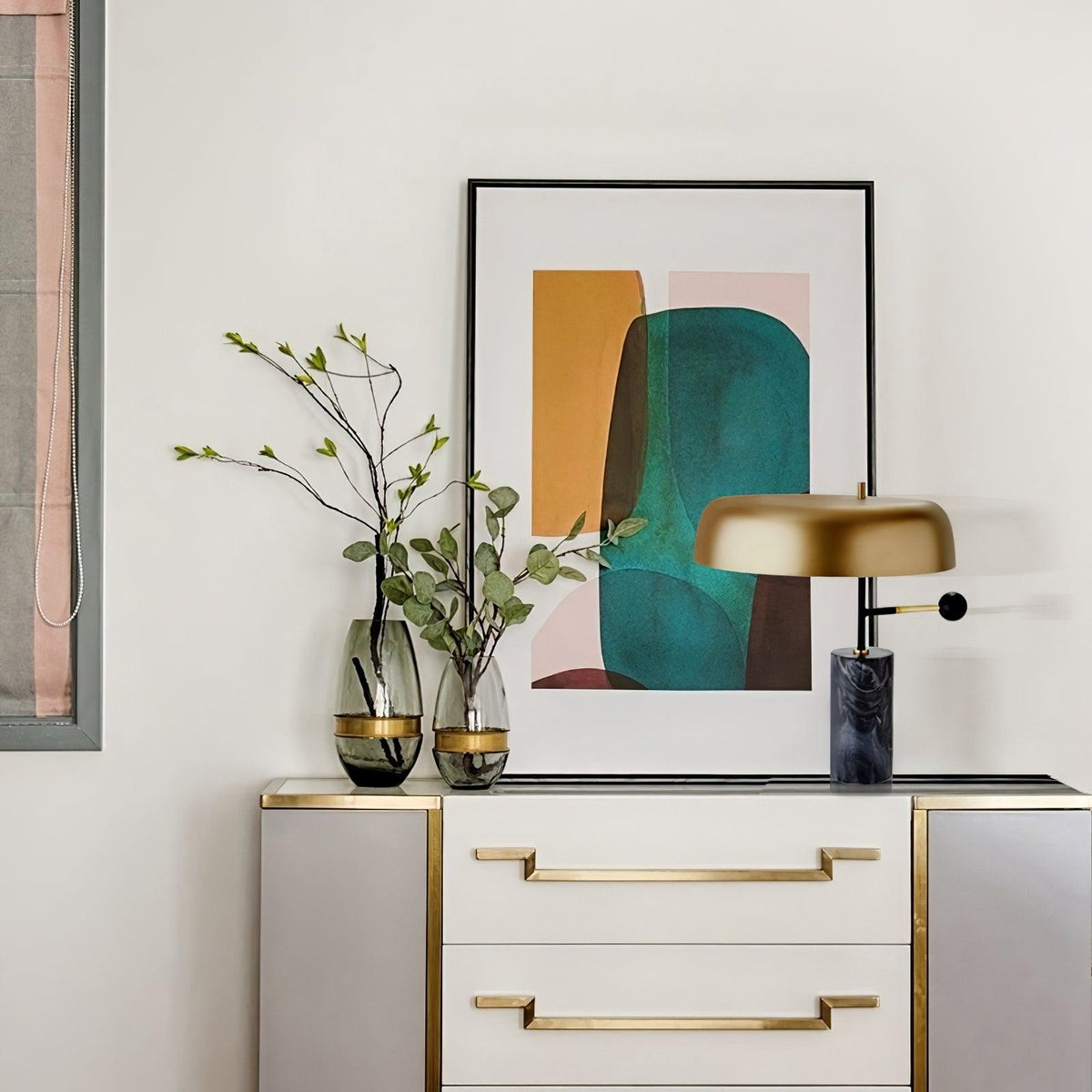 The Clérachic gold dome lamp lights a beige dresser with gold drawer pulls, framed art and glass vases behind it.