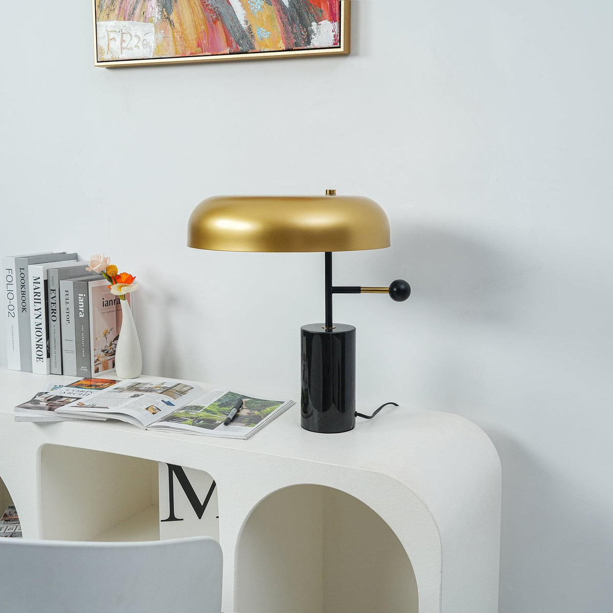 On a white console table, the Clérachic gold dome lamp stands beside stacked magazines under framed wall art.