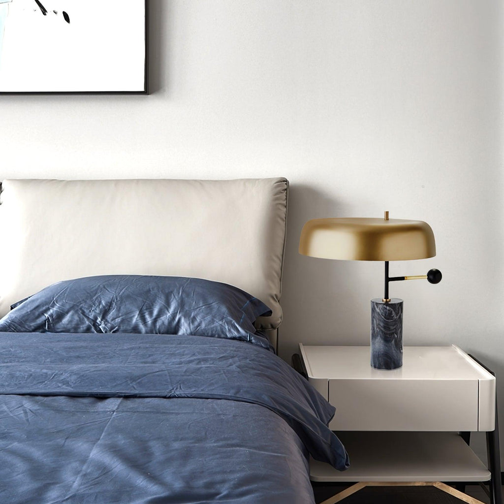 A wider view of the Clérachic bedside lamp, unlit, on a nightstand beside navy bedding and a plain headboard.