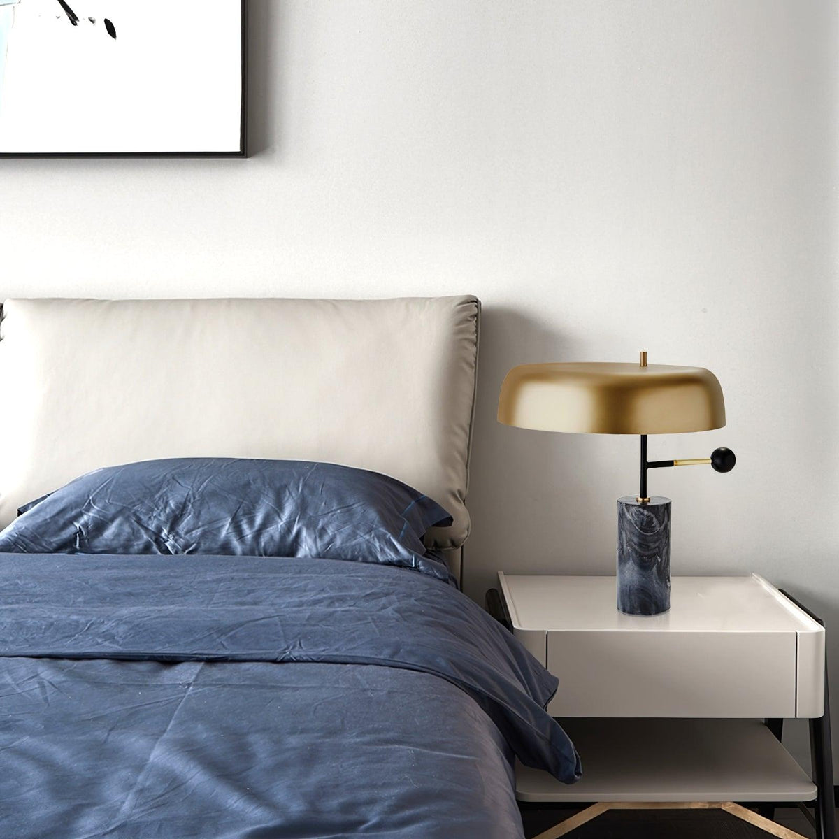 A wider view of the Clérachic bedside lamp, unlit, on a nightstand beside navy bedding and a plain headboard.