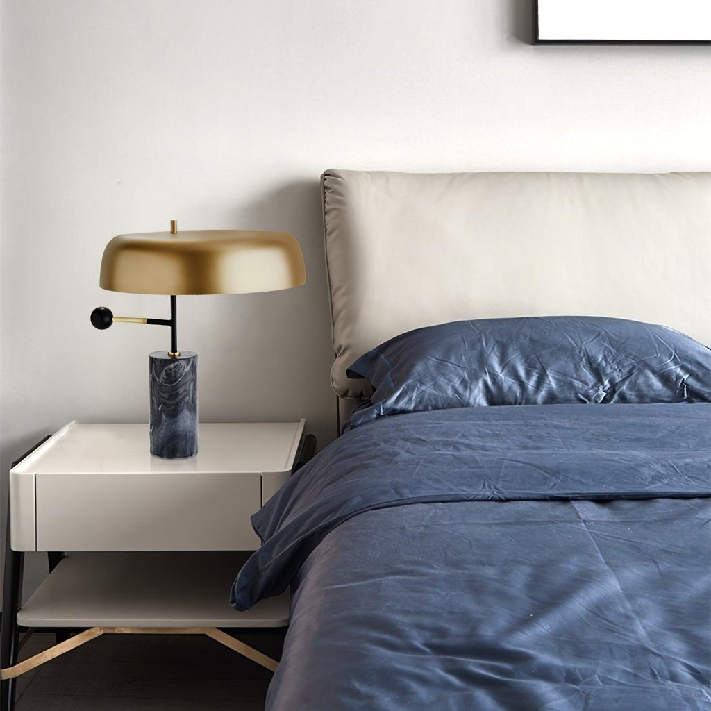 Clérachic's table lamp sits unlit on a bedside table next to a bed dressed in navy blue bedding and a white pillow.