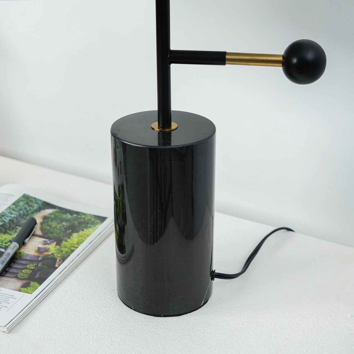 Close-up of the Clérachic lamp's black marble base and brass ball counterweight, with magazines blurred behind it.