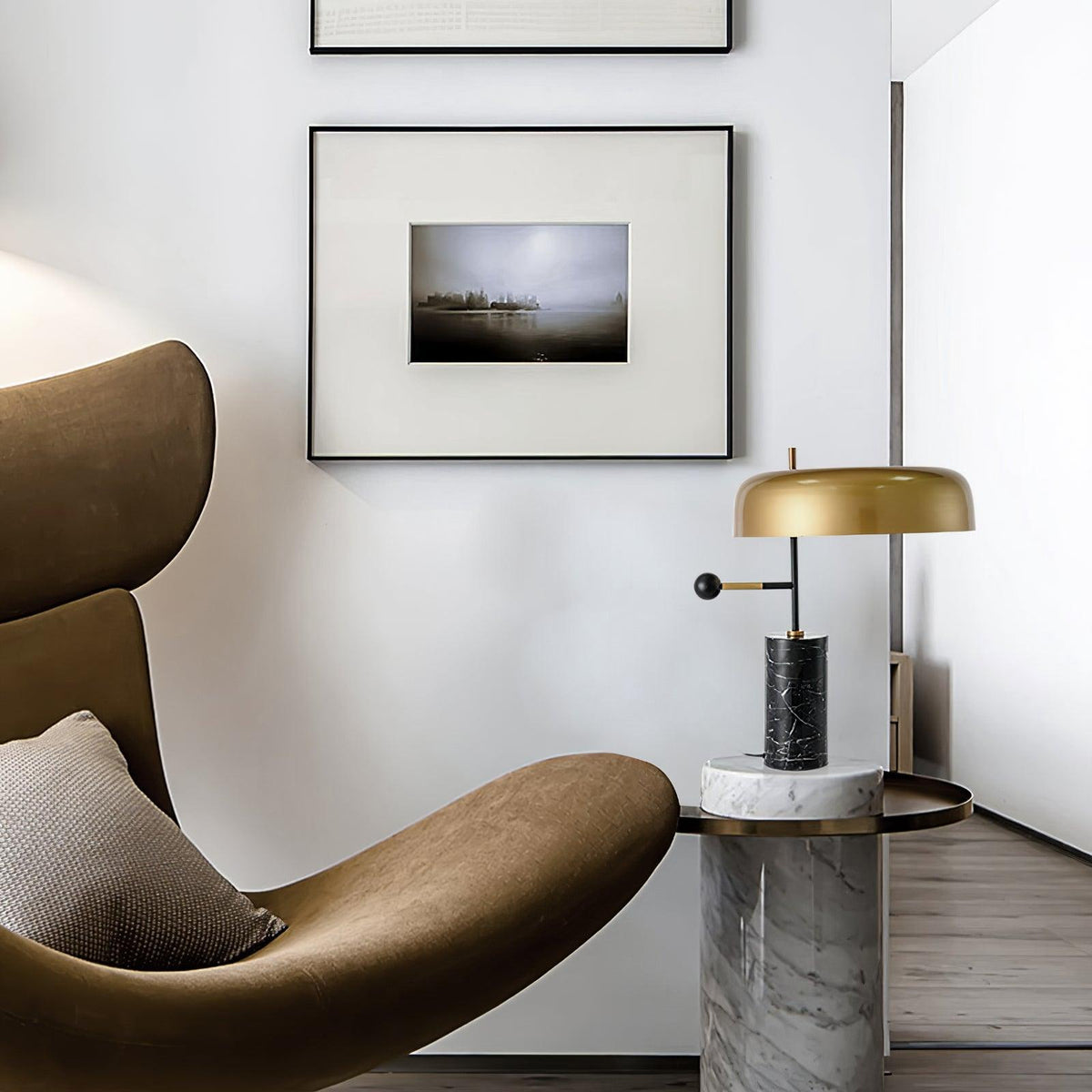 The Clérachic table lamp stands on a marble-topped side table beside a brown leather lounge chair and framed art.