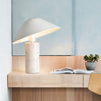 Clérachic white marble table lamp lit on a floating wooden shelf near a mirror, an open book and a small succulent.