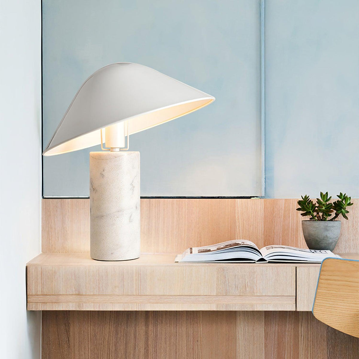 Clérachic white marble table lamp lit on a floating wooden shelf near a mirror, an open book and a small succulent.
