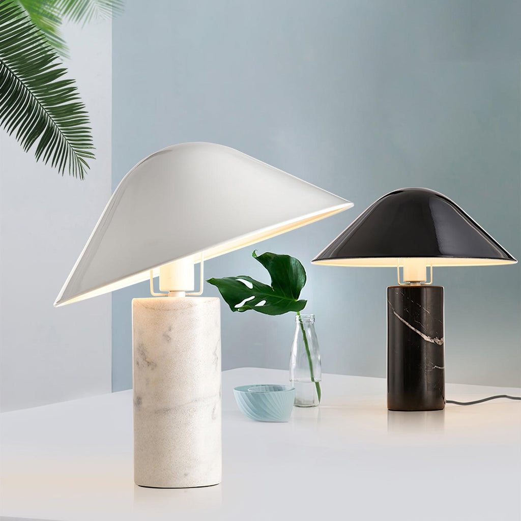 Two Clérachic table lamps, white marble in front and black marble behind, beside a monstera leaf sprig and a small blue bowl.