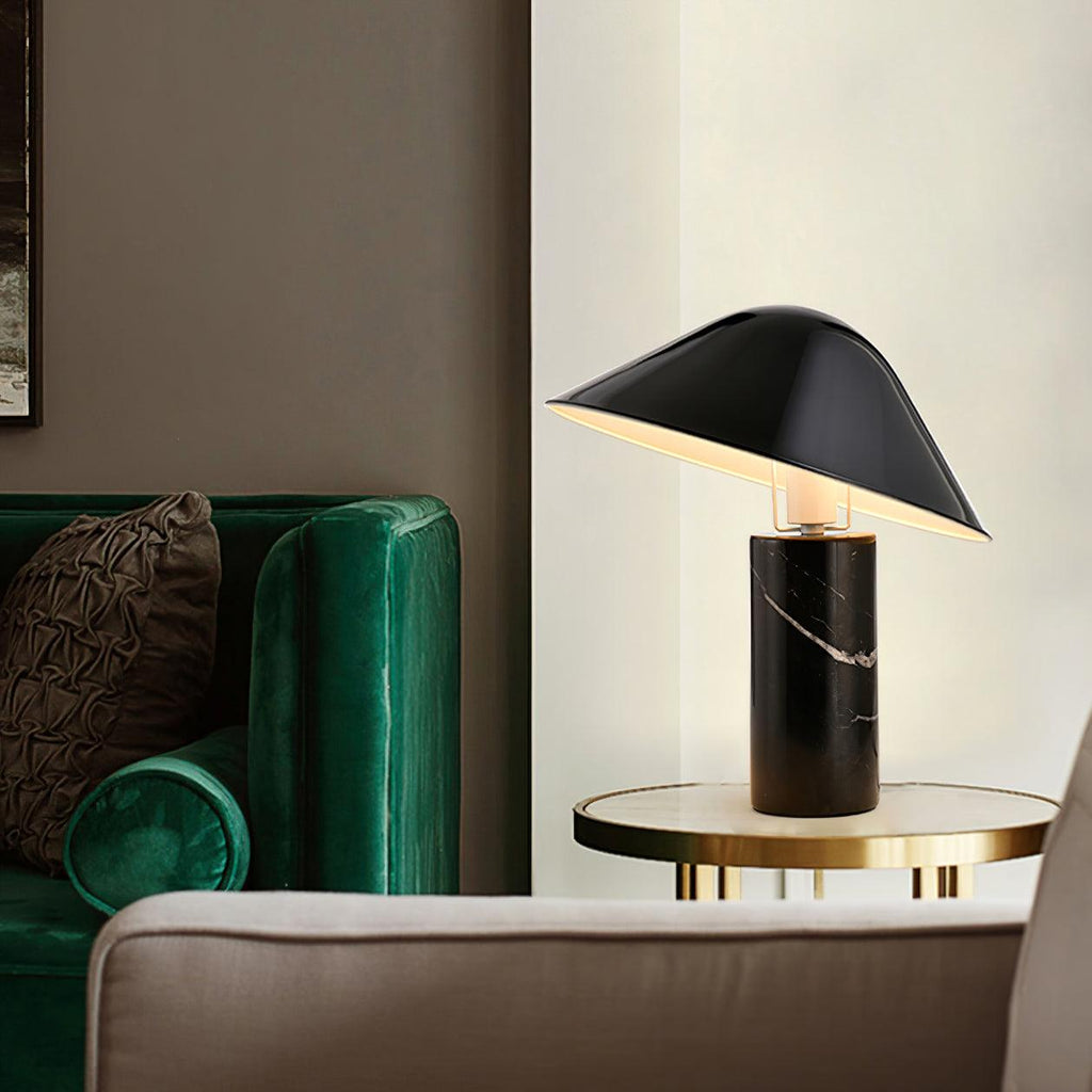Clérachic black marble table lamp lit on a round glass side table beside a green velvet sofa.