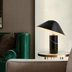 Clérachic black marble table lamp lit on a round glass side table beside a green velvet sofa.