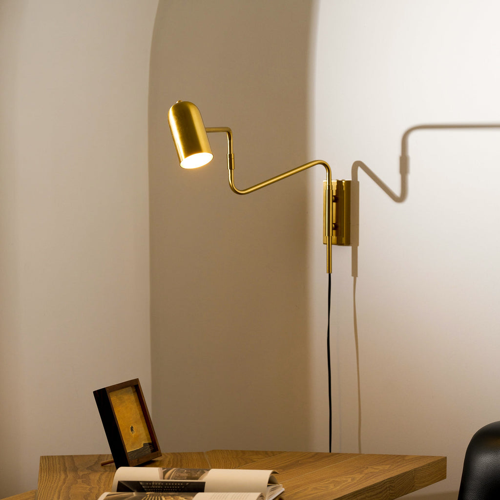 Swing arm wall lamp gold finish against a dark wall