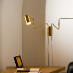 Swing arm wall lamp gold finish against a dark wall
