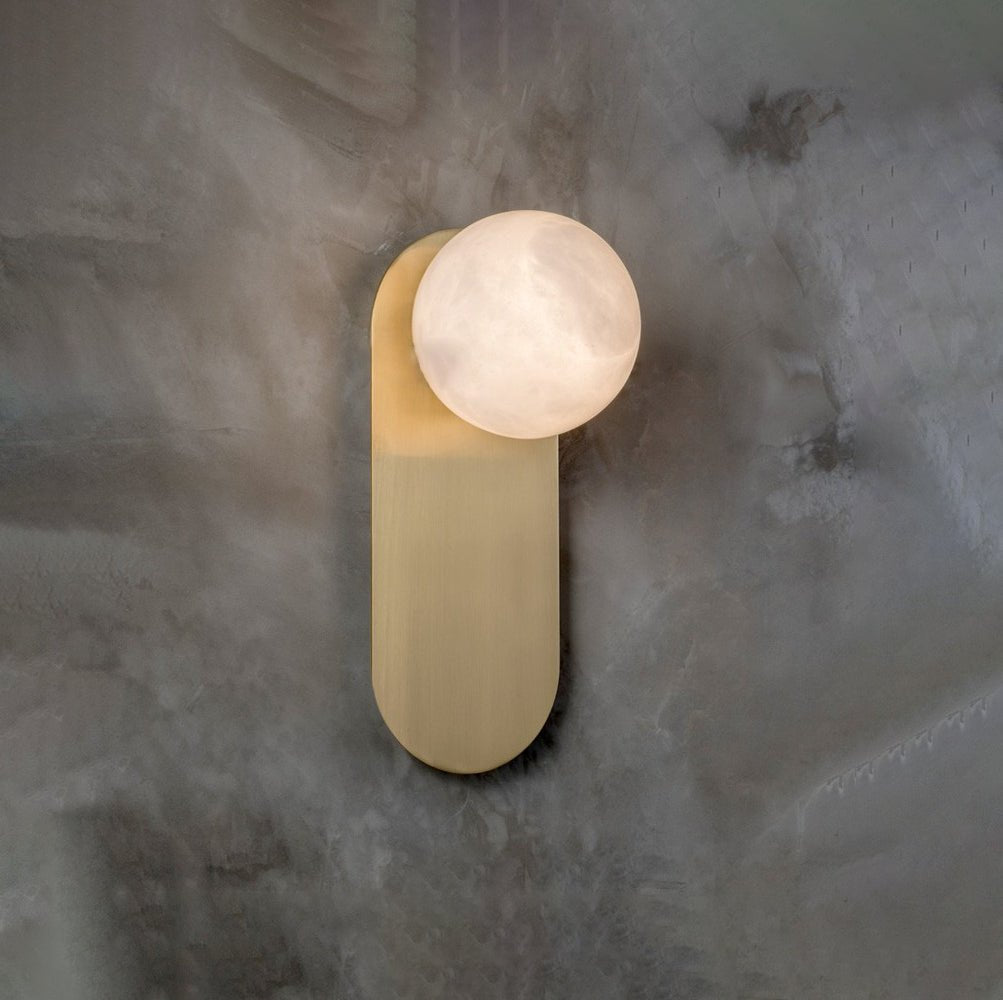 Adela wall sconce on a mottled grey plaster wall, the stone disc standing proud of the brass backplate