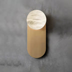 Straight-on view of the Adela sconce on grey concrete, veining visible across the hand-carved alabaster disc