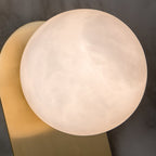 Close-up of the Adela sconce's alabaster disc, its cloudy stone grain filling the frame beside the brass plate