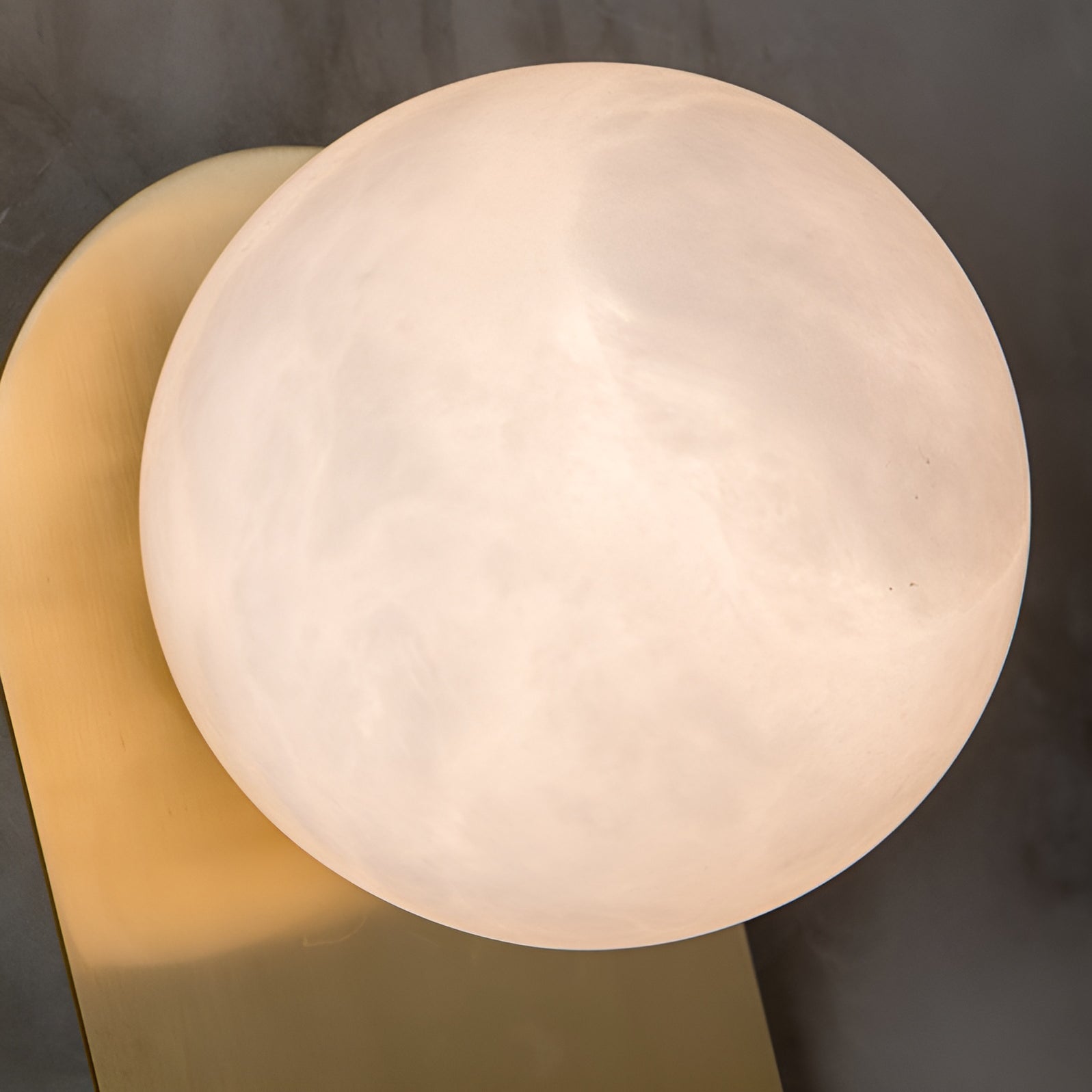 Close-up of the Adela sconce's alabaster disc, its cloudy stone grain filling the frame beside the brass plate