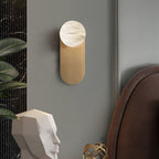 Adela wall sconce in a grey bedroom corner, framed closer beside a sculpted head and ribbed marble panel