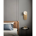 Wide bedroom view with the Adela sconce on a panelled grey wall above a round black bedside table