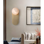 Adela wall sconce glowing warm in a living room beside a framed landscape painting and a cushioned sofa