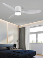 Wide white blades mark this Clérachic ceiling fan, glowing warm above a bedroom with a navy bed and sheer curtains.