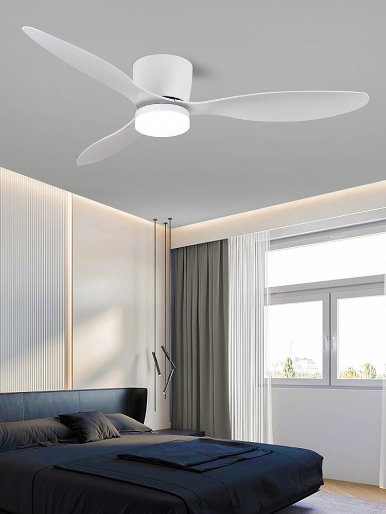 Wide white blades mark this Clérachic ceiling fan, glowing warm above a bedroom with a navy bed and sheer curtains.